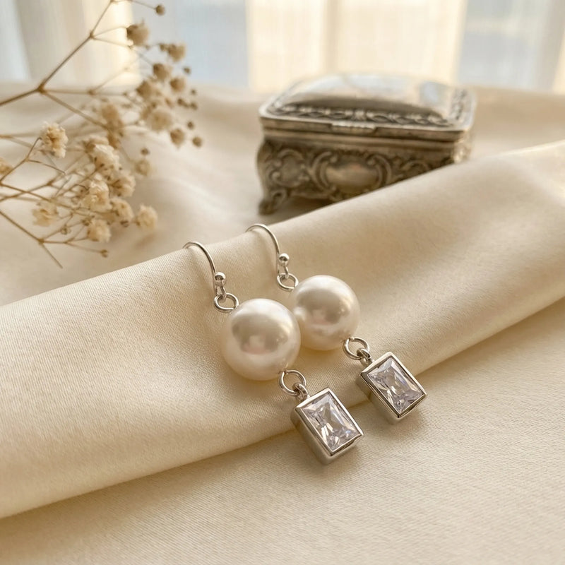 Elegant high-quality silver drop earrings featuring pearls and rectangular crystals resting on silk, representing pristine, tarnish-resistant jewelry.