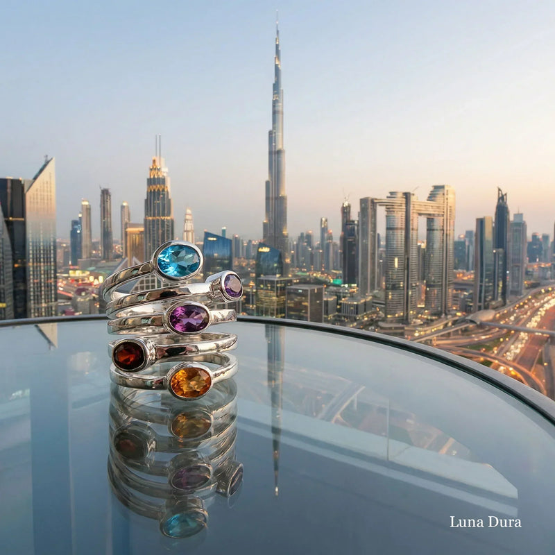 Luna Dura 925 sterling silver gemstone rings stacked on glass surface with Burj Khalifa and Downtown Dubai skyline at dusk