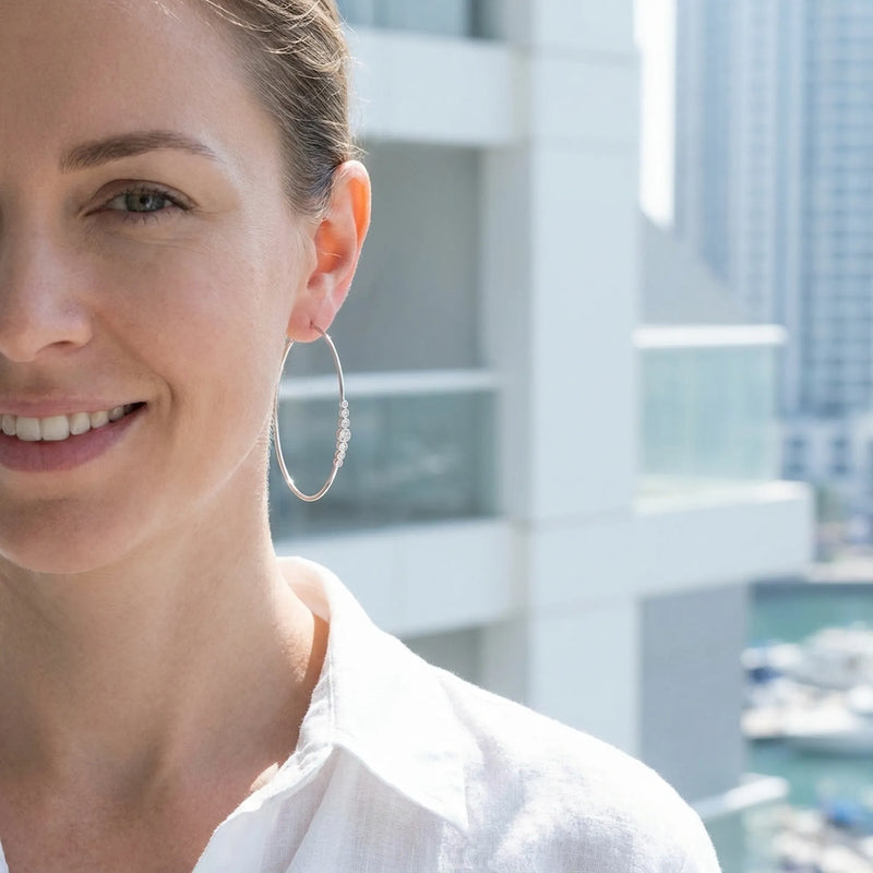 Smiling woman wearing extra-large CZ silver hoops by the water at Dubai Marina.