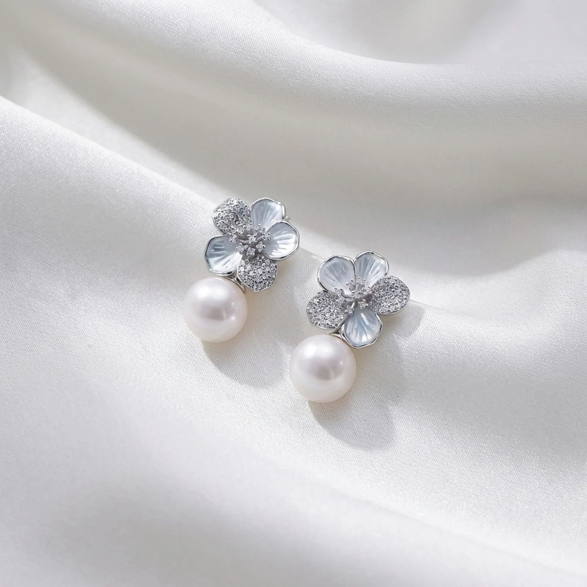 Close up of mother of pearl flower earrings ksa featuring pave CZ details and a premium faux pearl drop on white silk.