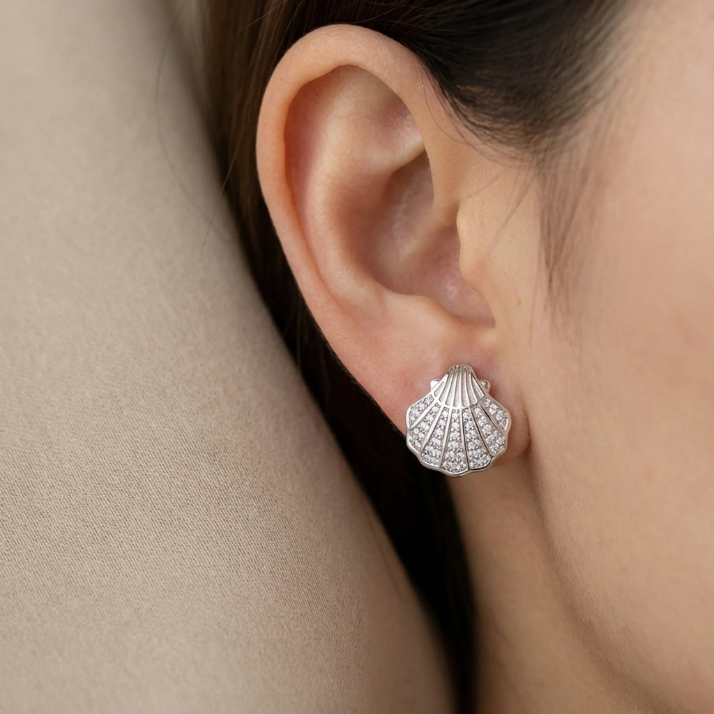 Model wearing petite silver shell CZ stud earrings styled in a softly lit Dubai interior.
