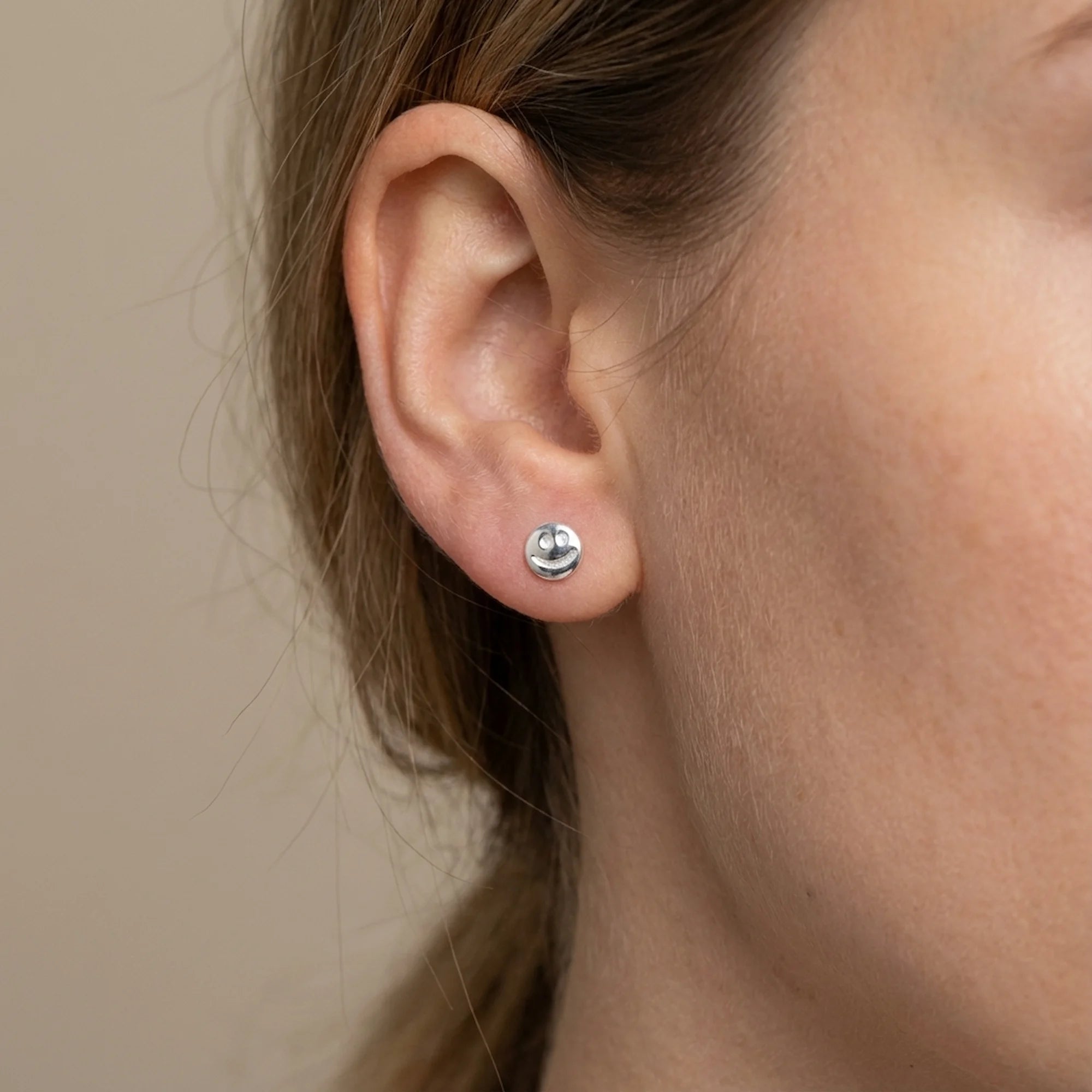Person wearing minimalist silver smiley face stud in Dubai