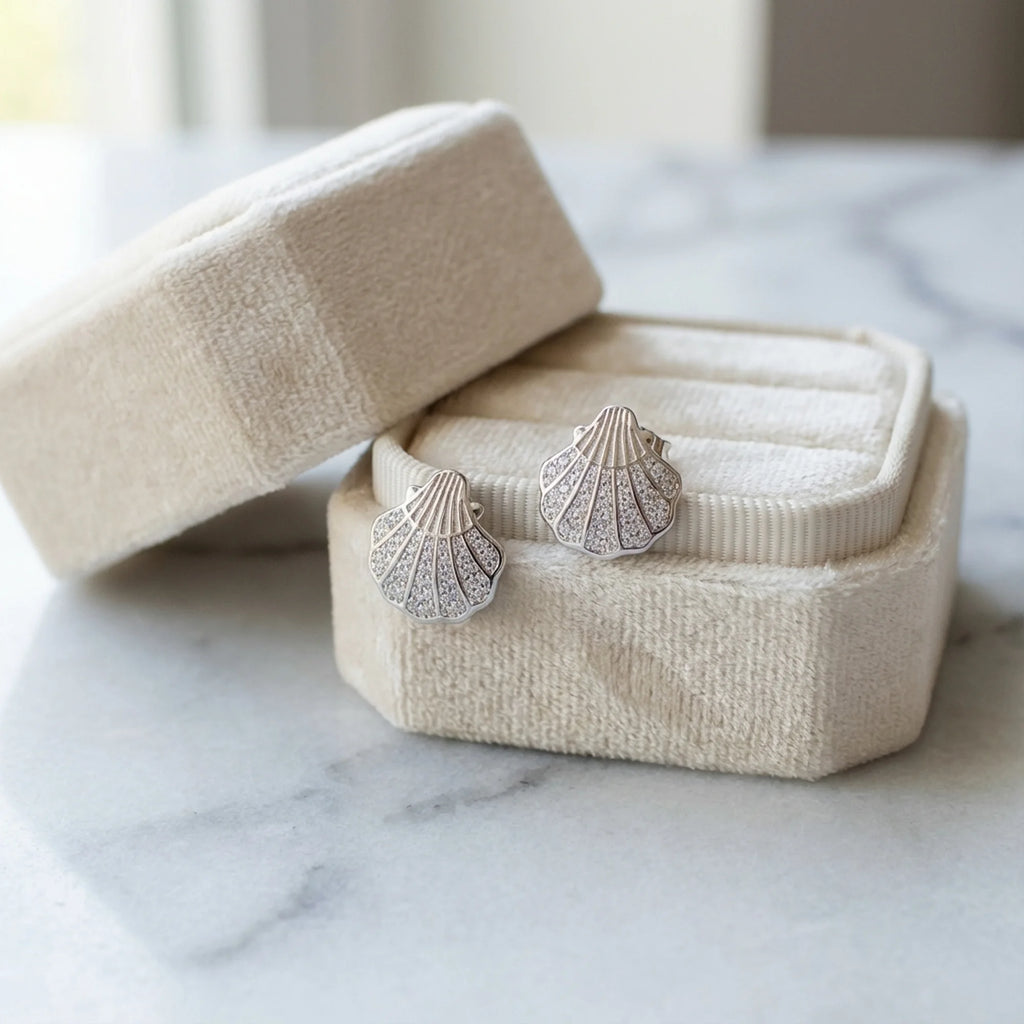 Silver shell earrings displayed inside a beige velvet presentation box resting on a marble surface in Dubai.