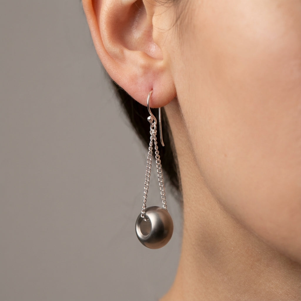 Silver earrings with dangling beads worn by a person against a neutral background