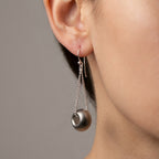 Silver earrings with dangling beads worn by a person against a neutral background