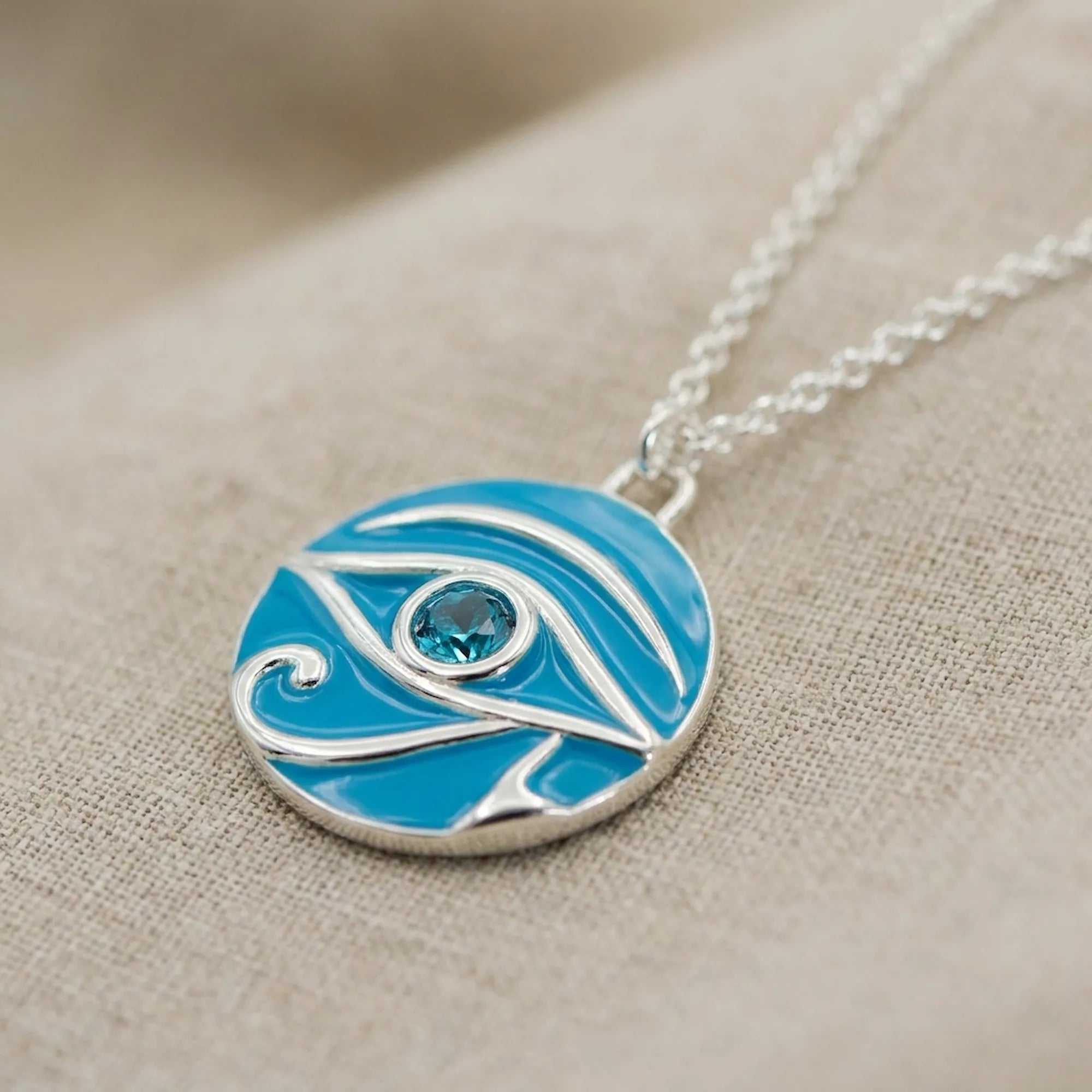 Macro details photo of Necklace with a blue and silver pendant on a beige fabric background 