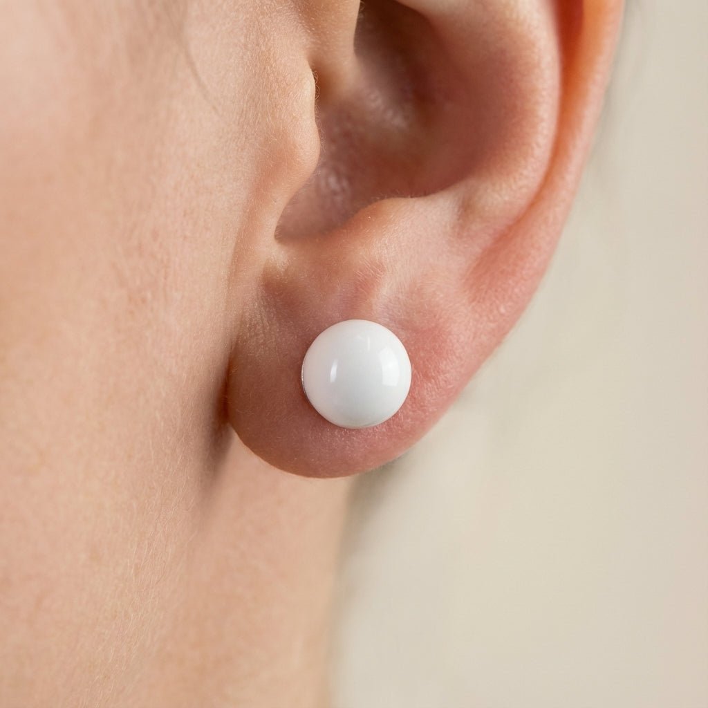 Close-up of a white stud earring on an ear against a neutral background 