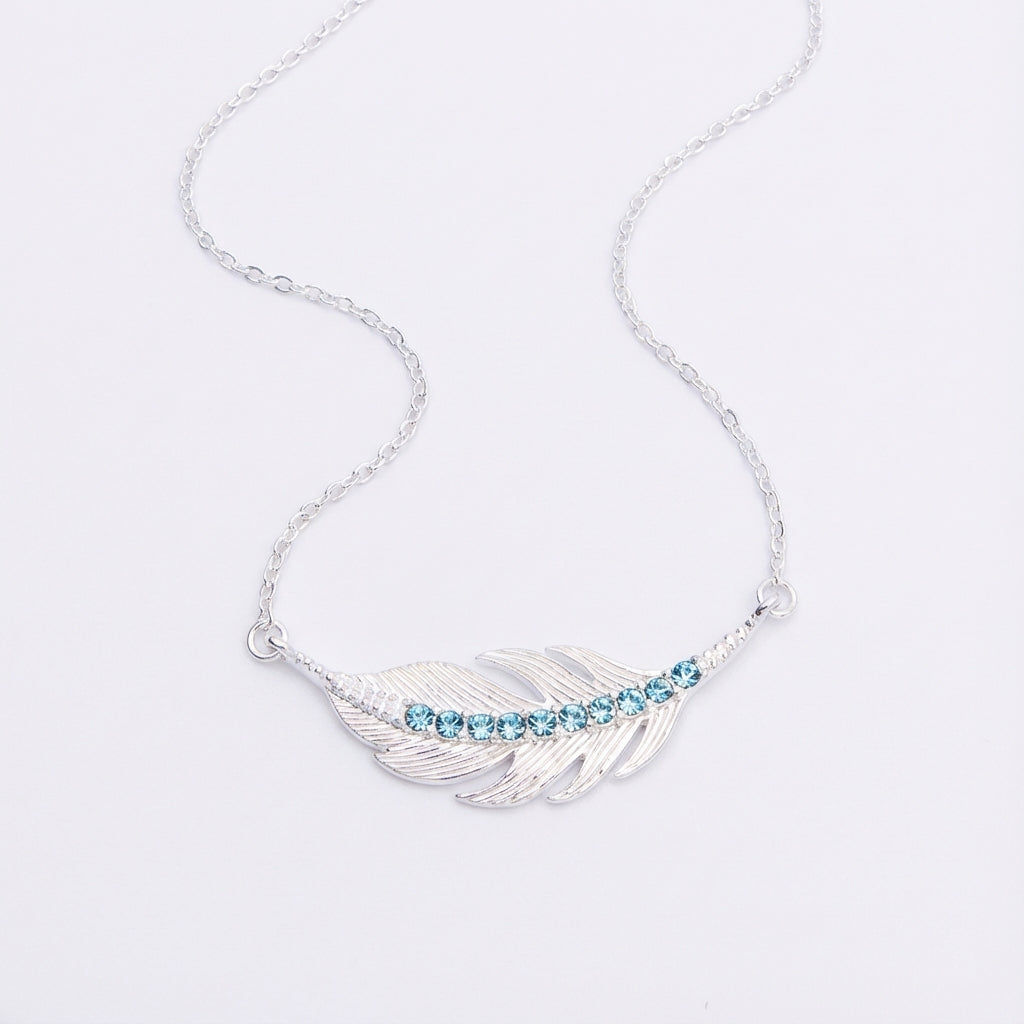 Angle photo of light weight Silver necklace with a feather-shaped pendant featuring blue stones on a light gray background UAE