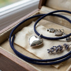 Sterling Silver 925  heart-shaped pendant on a blue cord with a wooden box and lavender flowers in the background.