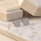 Square silver earrings with gemstones on a marble surface next to a jewelry box.