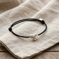 Black cord bracelet with a 925 silver heart charm on a beige fabric background
