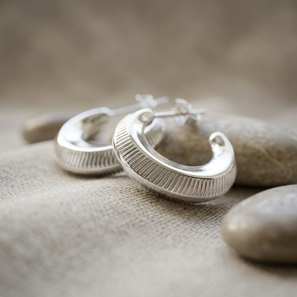 Ribbed 16mm 925 sterling silver crescent moon hoop earrings displayed on smooth stones in Dubai.