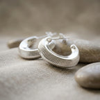 Ribbed 16mm 925 sterling silver crescent moon hoop earrings displayed on smooth stones in Dubai.