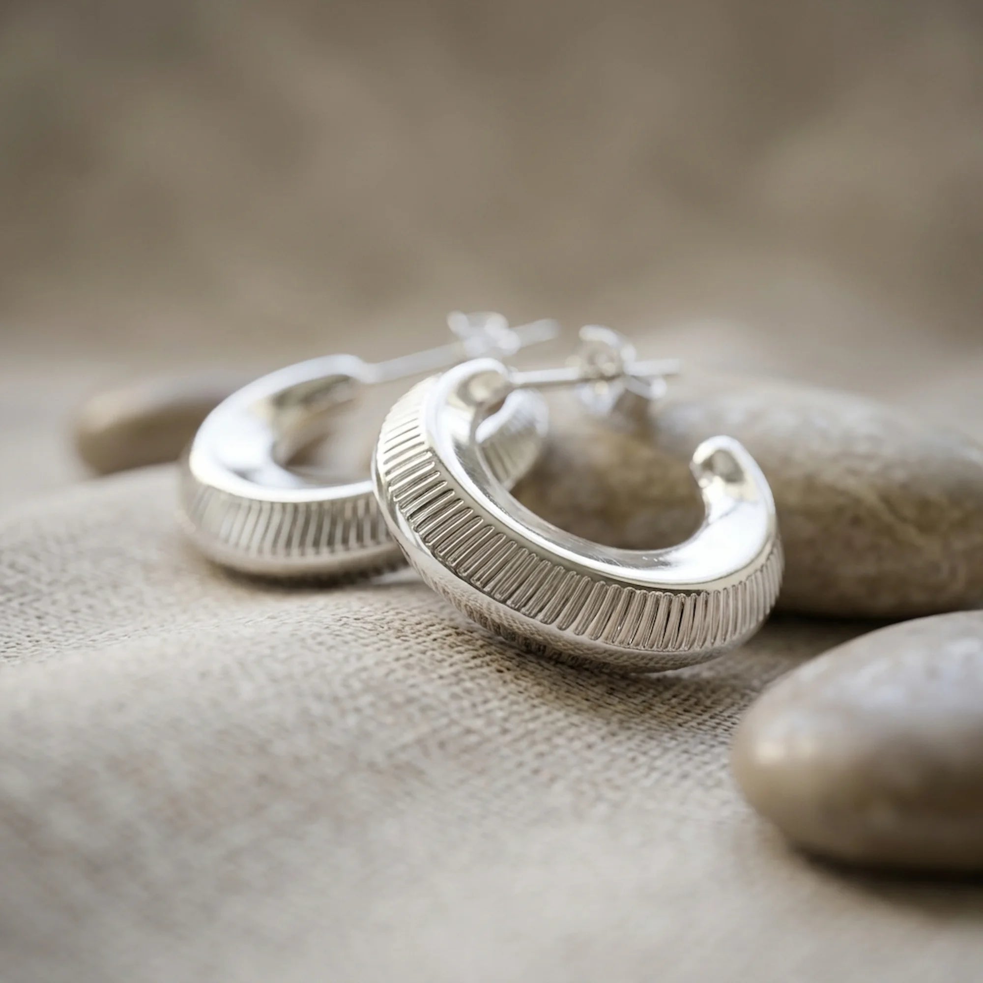 Ribbed 16mm 925 sterling silver crescent moon hoop earrings displayed on smooth stones in Dubai.
