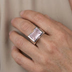 Hand wearing a ring to display size with a rose quartz gemstone on a neutral background