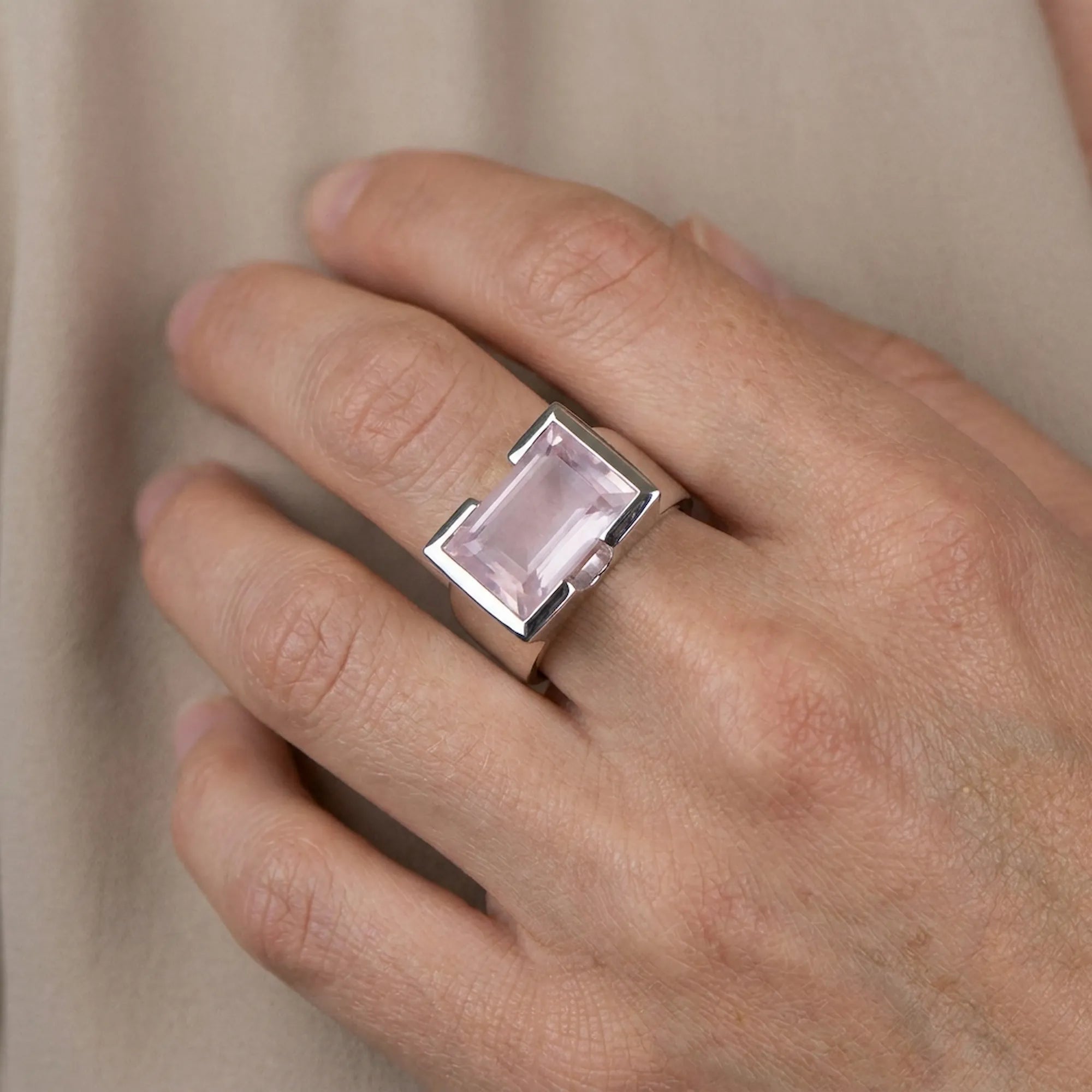 Hand wearing a ring to display size with a rose quartz gemstone on a neutral background