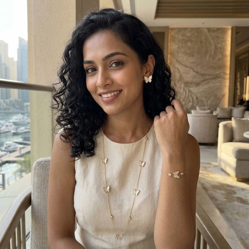 Woman smiling while wearing 18K gold plated mother of pearl butterfly station necklace, studs, and bracelet in Dubai.
