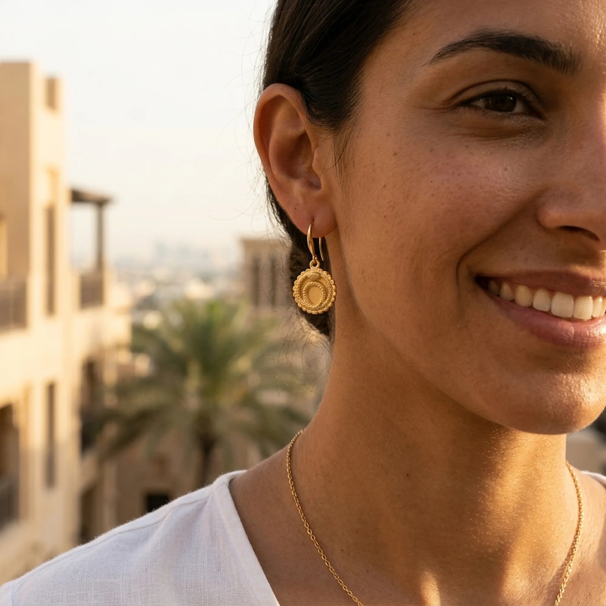 Close-up of a woman wearing the nickel-free 18K gold vermeil ouroboros drop earrings outdoors in Dubai.