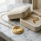 18K gold vermeil ouroboros station necklace resting on marble surface next to its open beige velvet jewelry box.