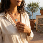 Woman wearing a necklace with a scenic background of blue sea and olives tree 