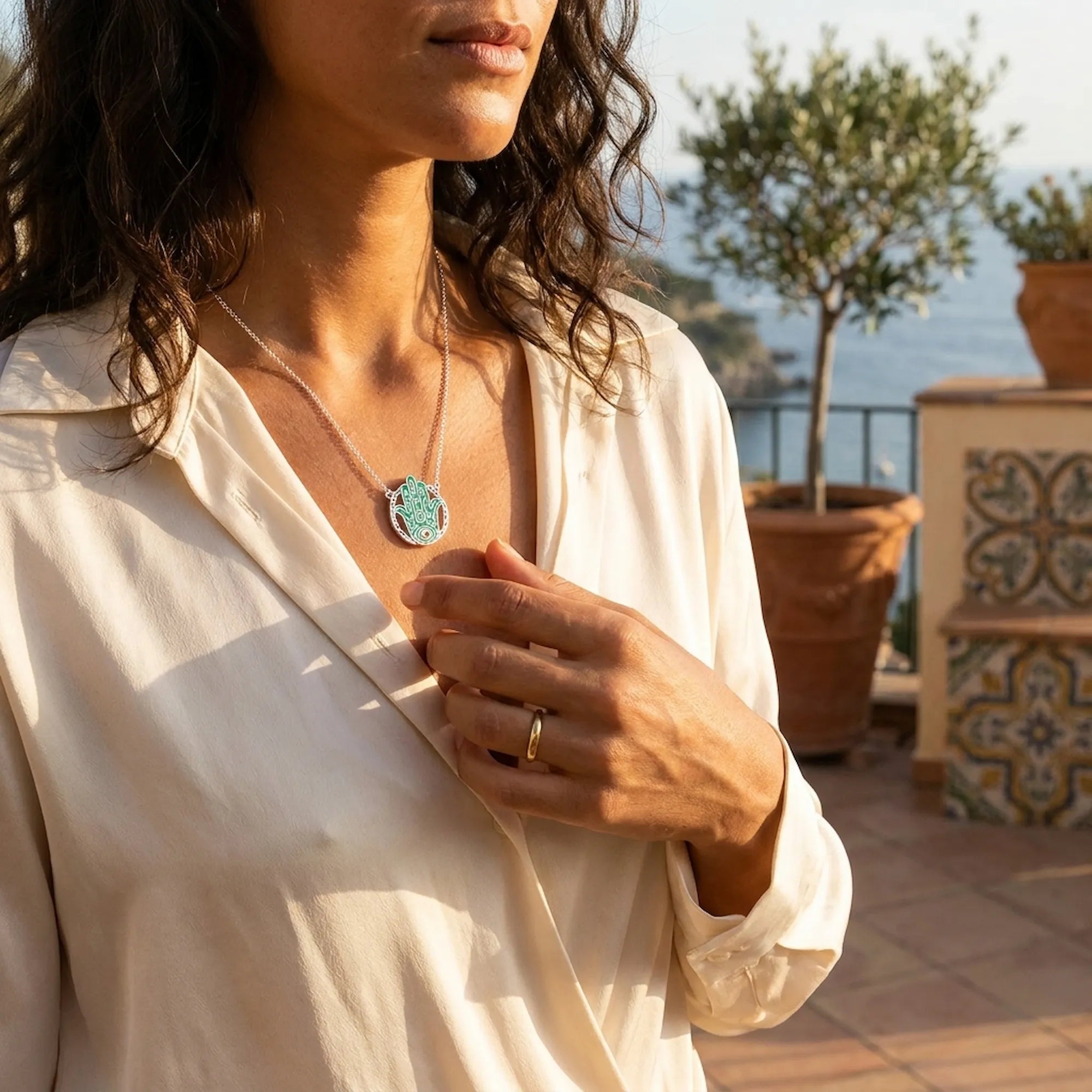 Woman wearing a necklace with a scenic background of blue sea and olives tree 