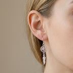 Silver earring with feather detail worn by a model against a neutral background at Luna Dura studio SZR.