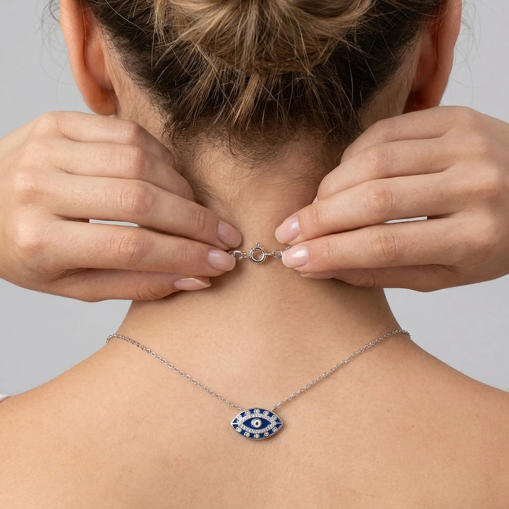 Model wearing a silver necklace with an eye pendant, adjusting closer clasp on a neutral background
