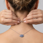 Model wearing a silver necklace with an eye pendant, adjusting closer clasp on a neutral background