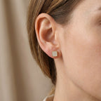 Close-up of a person wearing gold square stud earrings with a neutral background UAE