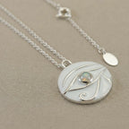 Macro photo of silver necklace with a circular pendant featuring an opal stone on a beige background