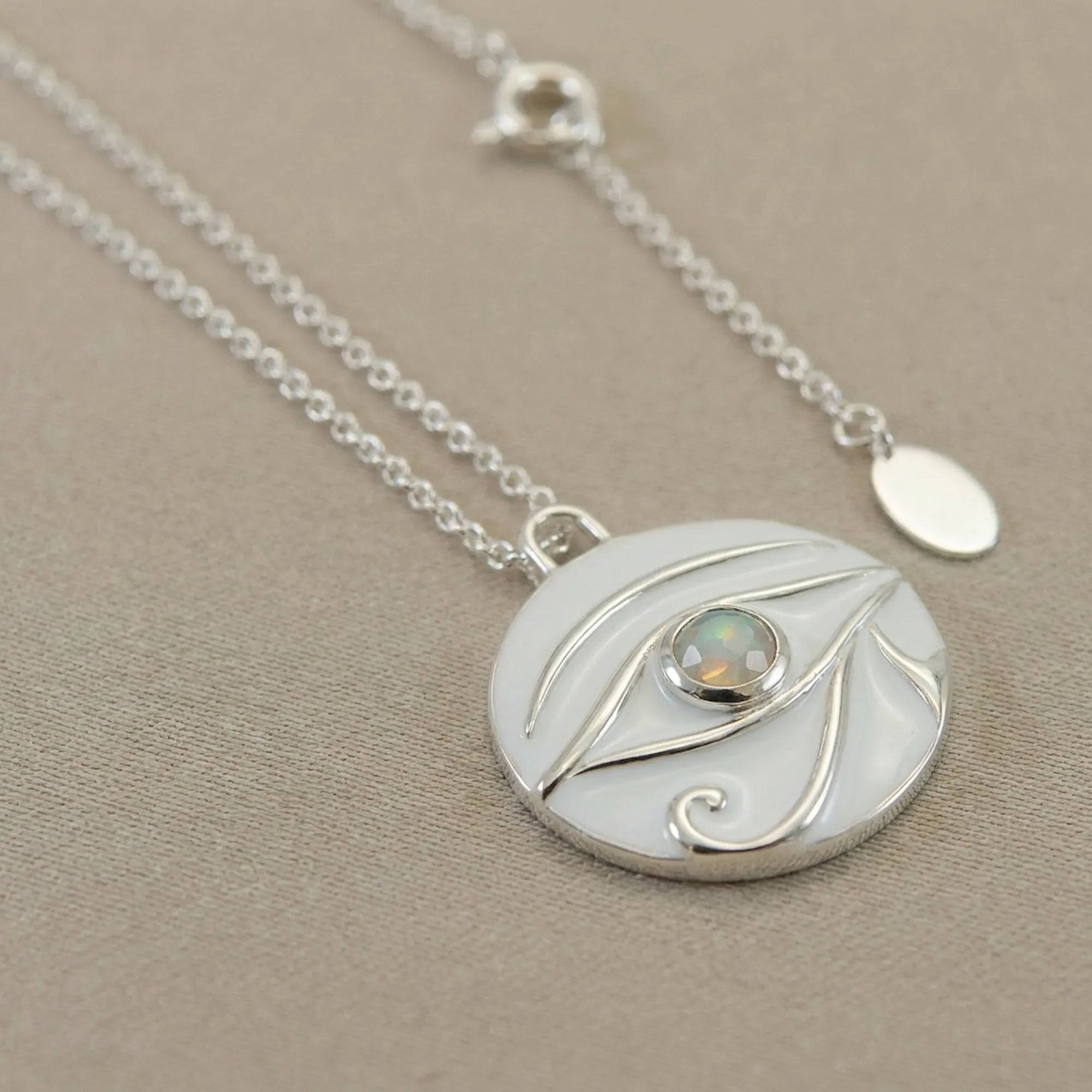 Macro photo of silver necklace with a circular pendant featuring an opal stone on a beige background