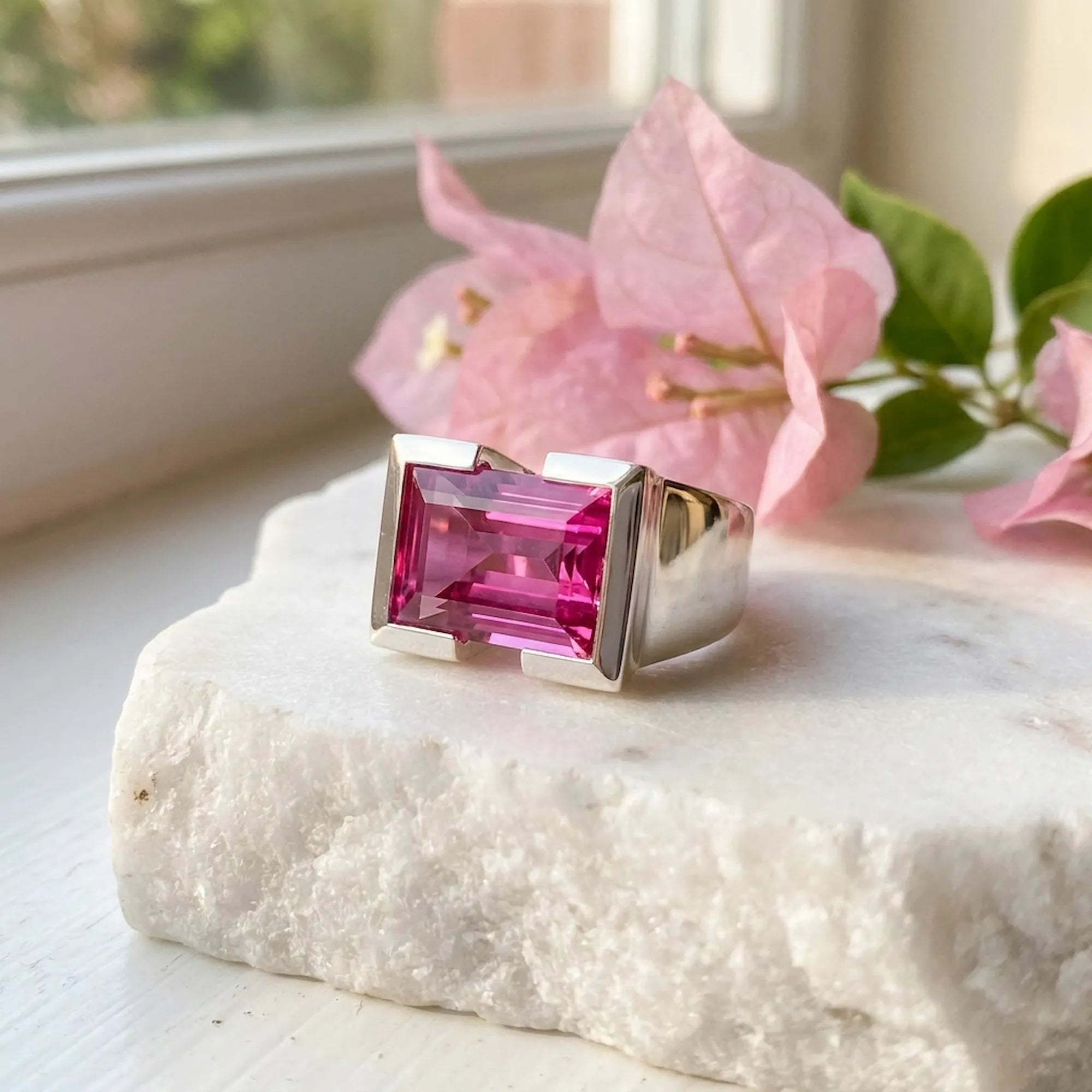 Macro photo 925 silver ring with gemstone displayed over marble with rose color flower blurred in the background 