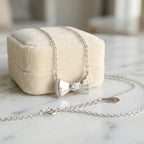 A 925 silver bow necklace resting on a beige velvet jewelry box on a marble surface, available in Dubai.