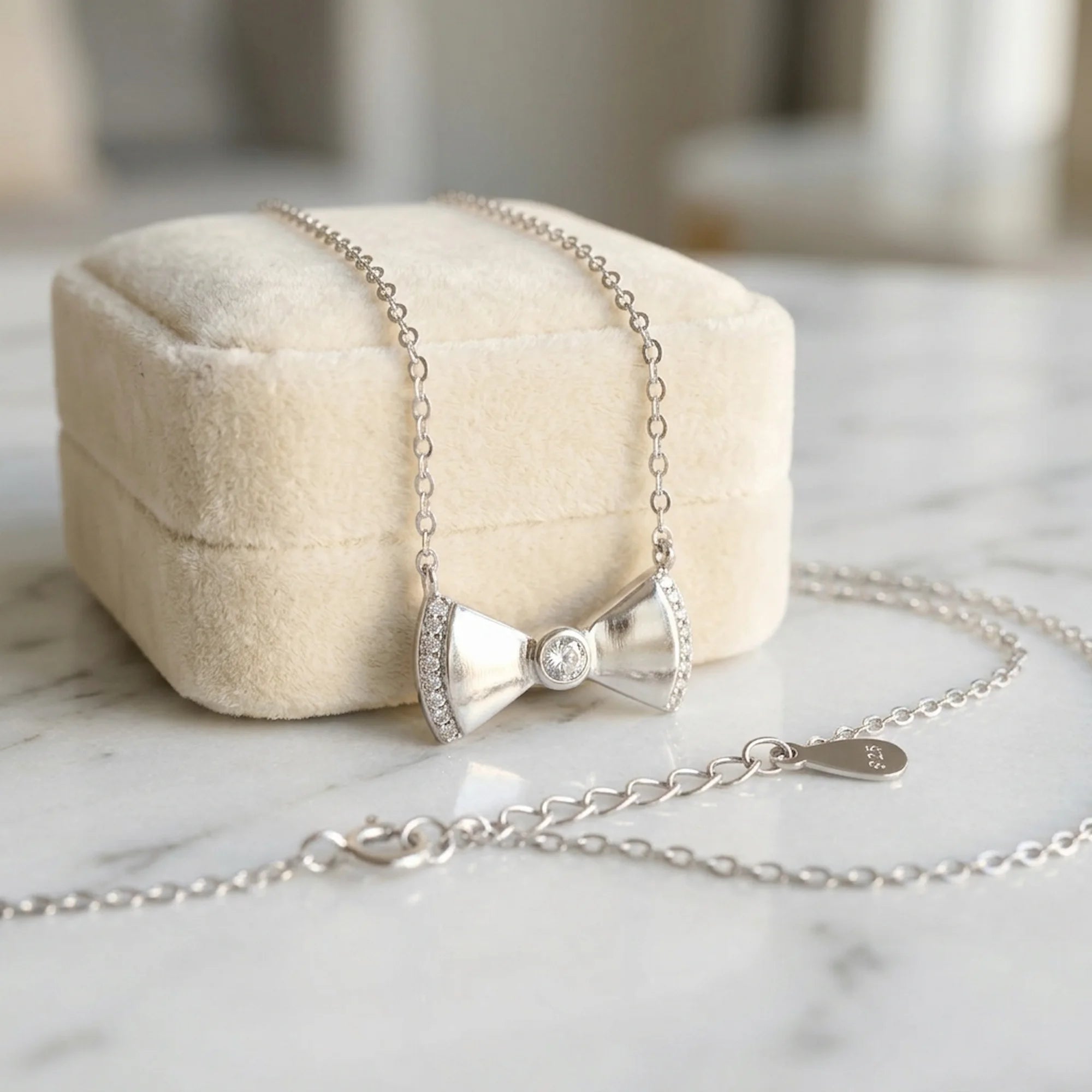 A 925 silver bow necklace resting on a beige velvet jewelry box on a marble surface, available in Dubai.