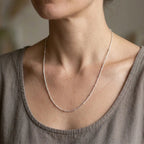 Woman wearing a delicate silver-tone necklace with spaced bead stations and a taupe top.