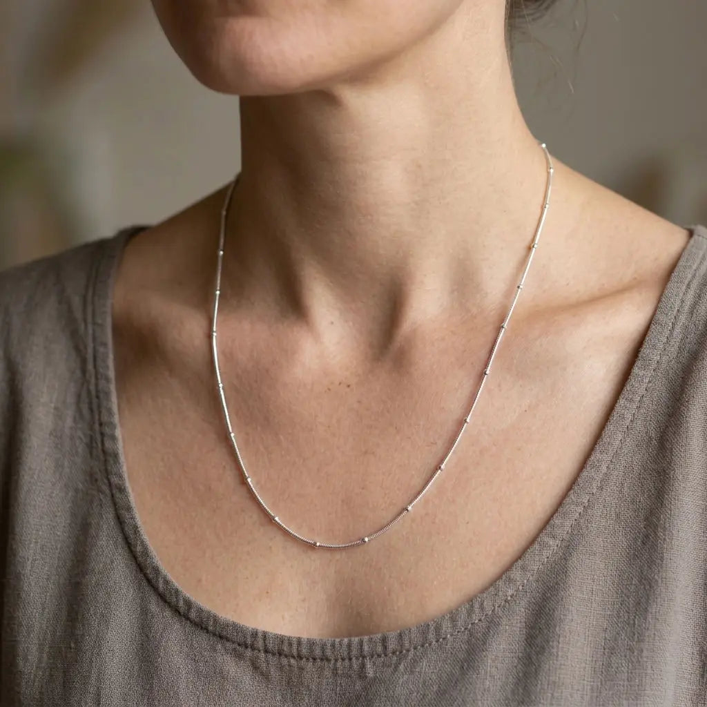 Woman wearing a delicate silver-tone necklace with spaced bead stations and a taupe top.