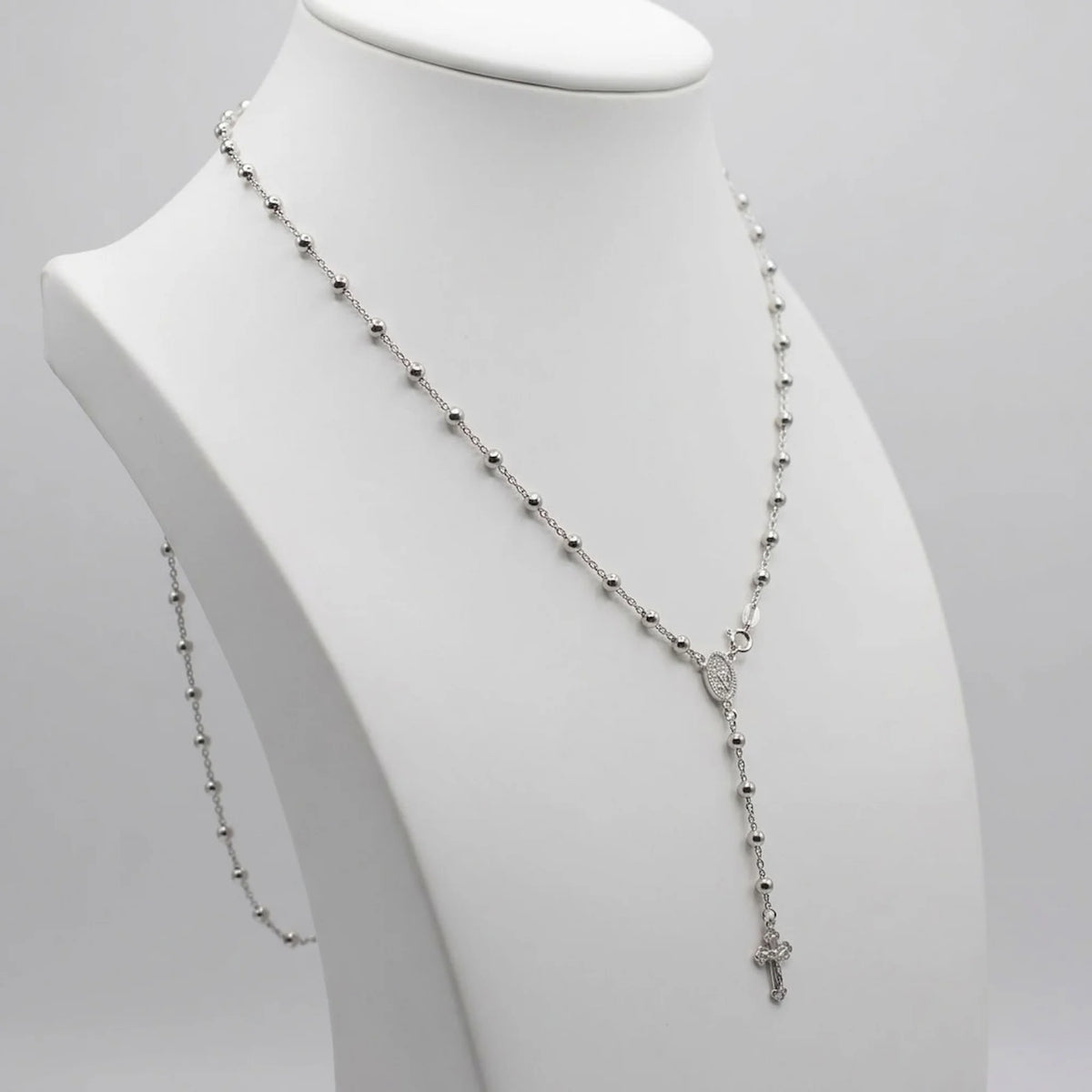 Rhodium-plated 925 silver rosary necklace on a white display bust, showing the beaded chain, Marian medal and Y-drop crucifix.