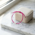 Fuchsia Pink bracelet in Dubai with a 925 silver charm on a beige jewelry box on a marble surface.