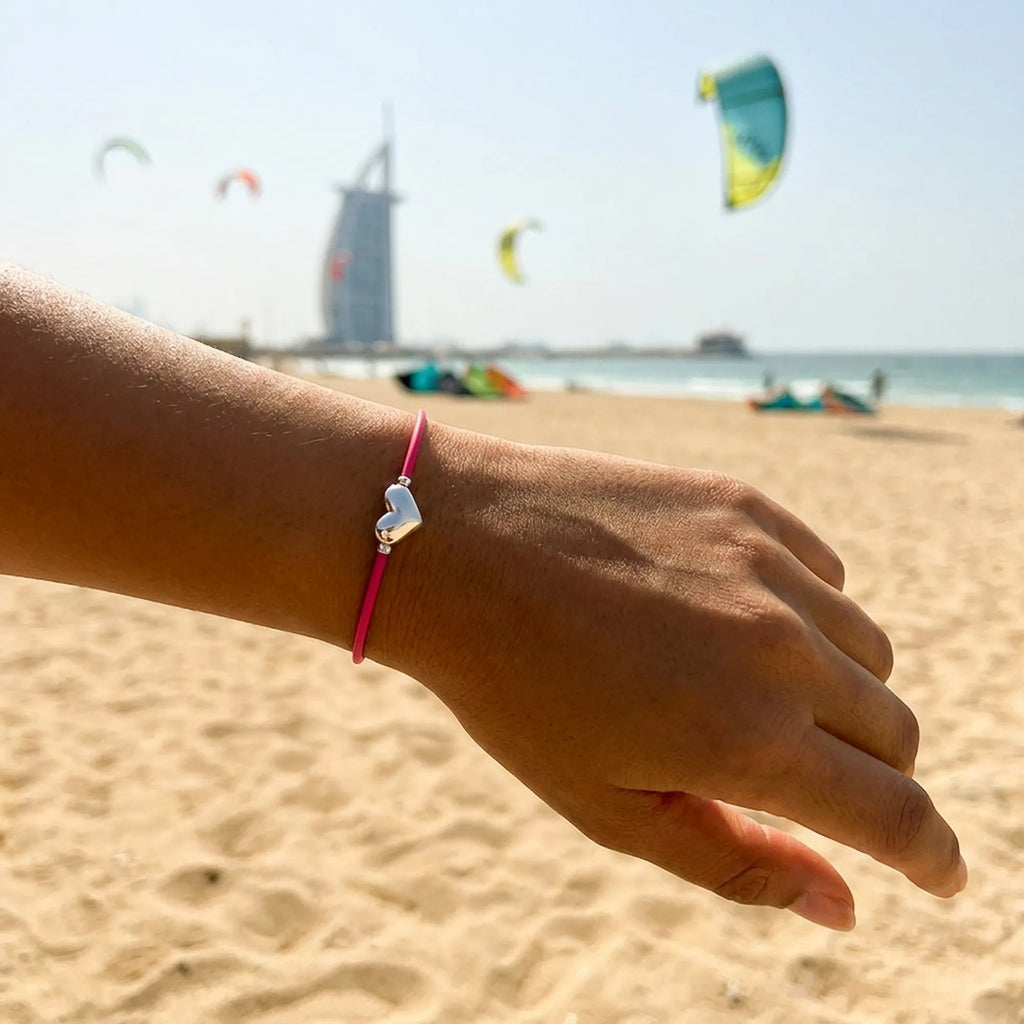 Pink cord silver heart bracelet on the wrist with Burj Al Arab and kitesurfers behind