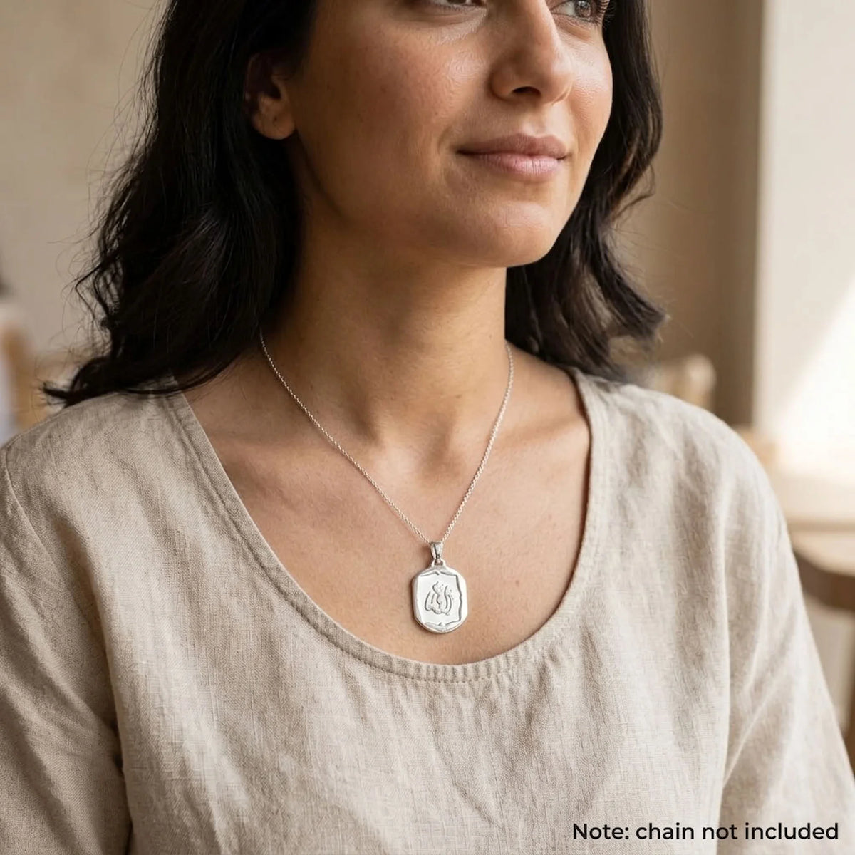 Woman wearing a shield-shaped Allah silver charm pendant with a polished frame; chain shown for styling only.