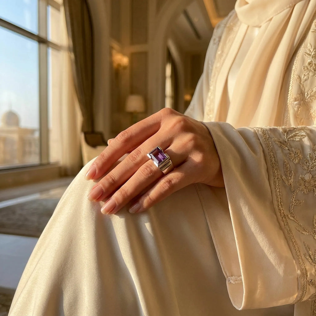Hand wearing amethyst cocktail ring in embroidered abaya at Emirates Palace Abu Dhabi with golden palatial interior