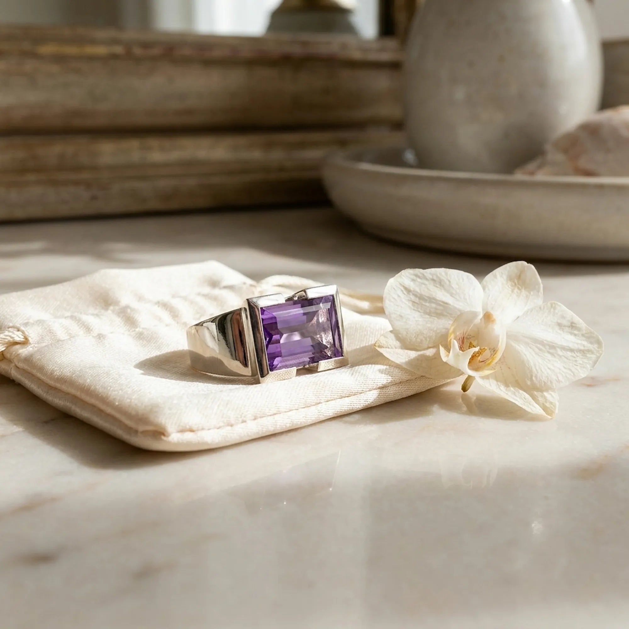 Natural amethyst cocktail ring on cream cotton pouch beside white orchid on warm marble surface in soft natural light