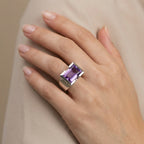 Close-up of hand wearing 8.15 carat natural amethyst baguette cocktail ring in 925 sterling silver, taupe background