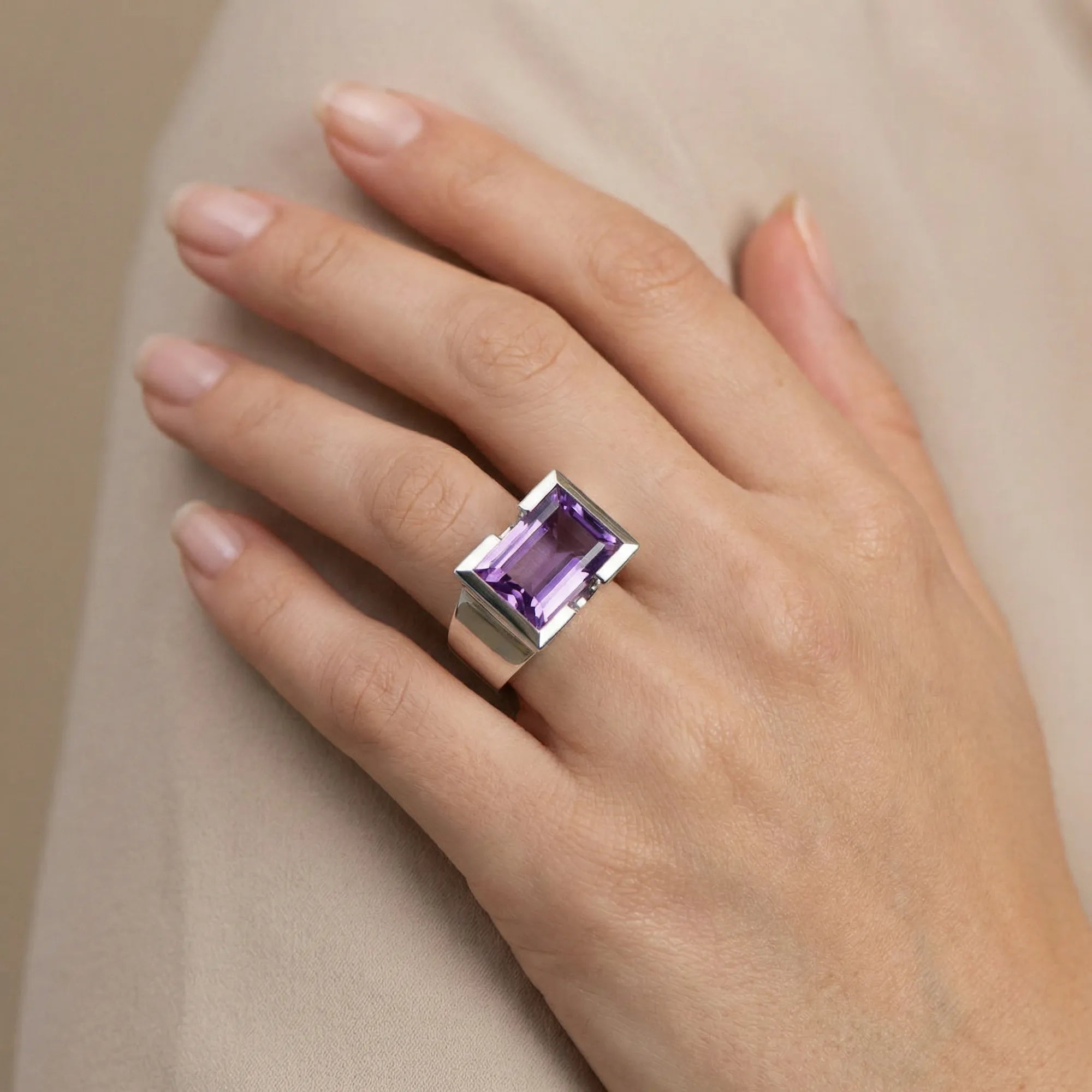Close-up of hand wearing 8.15 carat natural amethyst baguette cocktail ring in 925 sterling silver, taupe background