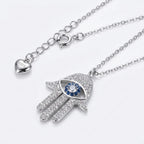 Silver necklace with Hamsa hand pendant featuring a blue gemstone on a white background