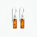 Pair of cognac Baltic amber cylinder drop earrings with sterling silver French hooks, displayed on a clean white background