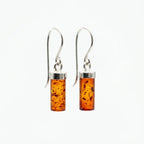 Pair of cognac Baltic amber cylinder drop earrings with sterling silver French hooks, displayed on a clean white background