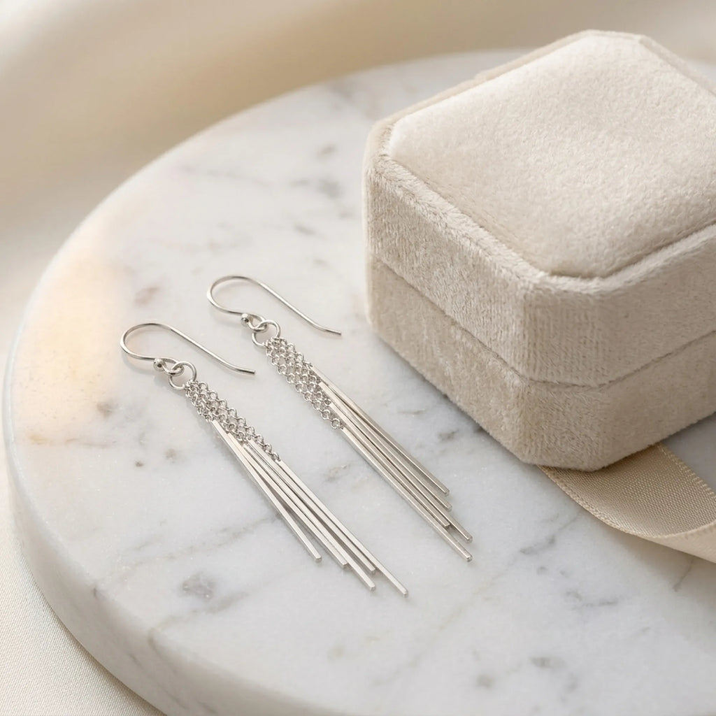 Sterling silver bar drop earrings on marble beside a cream jewelry gift box.