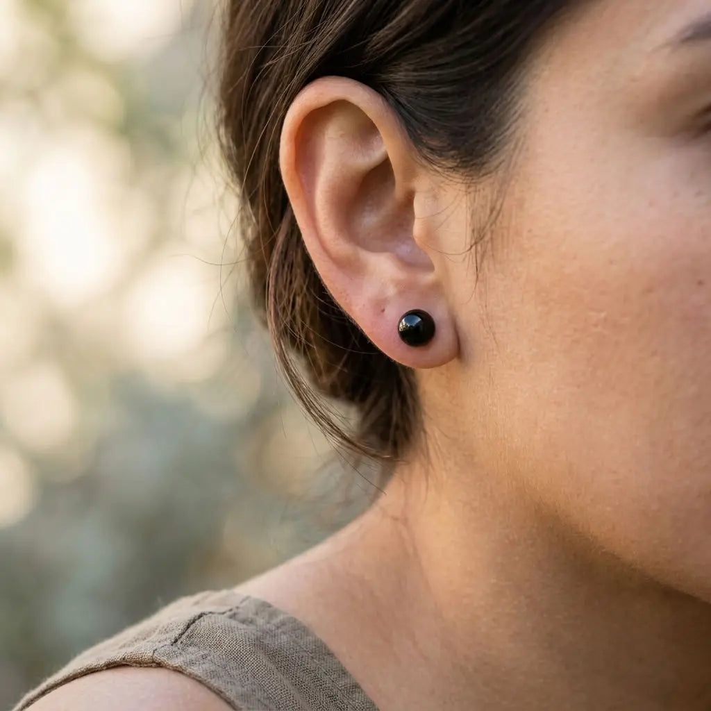 Single glossy black resin ball stud earring worn on the earlobe, showing the rounded 10 mm silhouette.