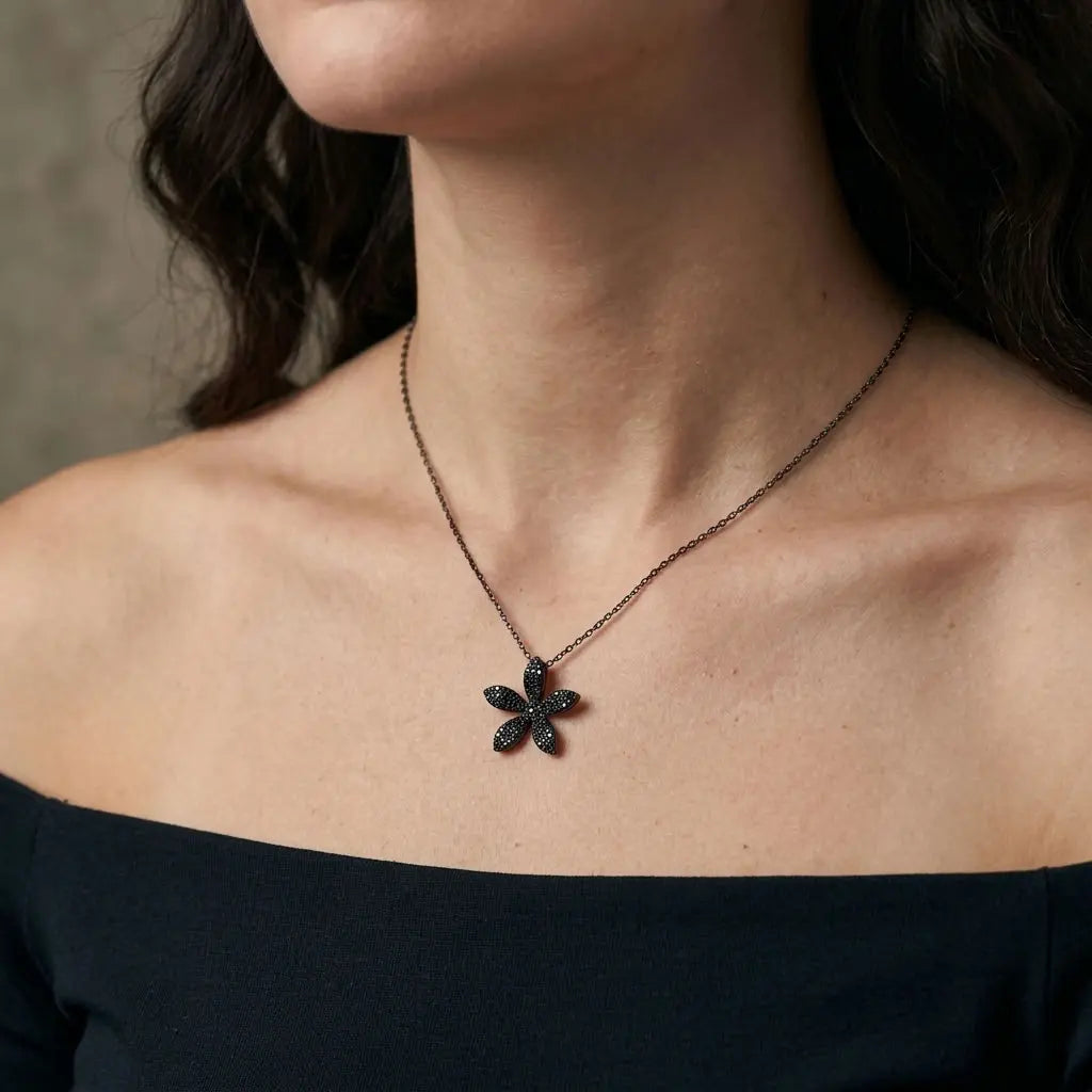 Black cubic zirconia five-petal flower necklace worn at the neckline above a black off-shoulder top.